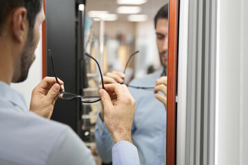 Man trying on eyeglasses before the mirror in optical shop