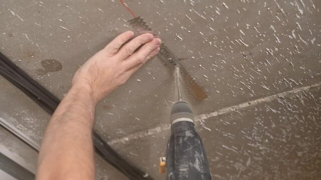 Worker drills a hole in the ceiling with a hammer drill to install the ceiling profile fixing. Installation of plasterboard ceiling. Renovation or reconstruction of the building. Close-up, live video