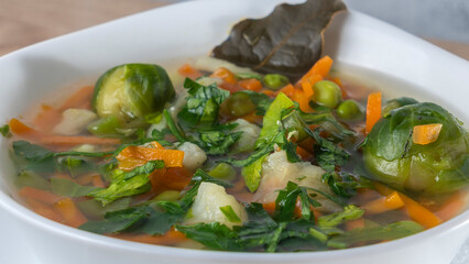 Fresh vegetable soup made of green bean, pea, carrot, potato, red bell pepper, tomato and leek in bowl.