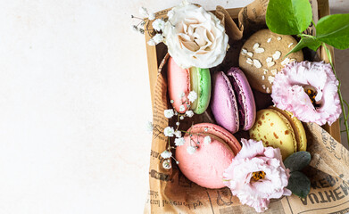 Various types of colorful macarons or macaroons decorated with flowers on light background. Traditional french almond dessert with sweet filling. Top view.