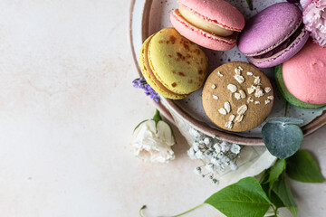 Various types of colorful macarons or macaroons decorated with flowers on light background. Traditional french almond dessert with sweet filling. Top view.