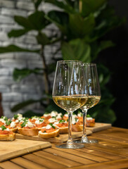 Toast or bruschetta with tomatoes, mozzarella and basil and two glasses with white wine. An appetizer for a banquet or buffet.