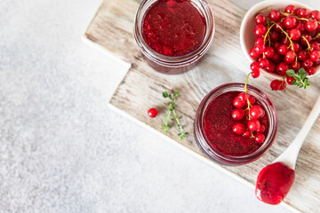 Homemade red currant jam or jelly in glass jars and red currants fresh berries on wooden cutting board.