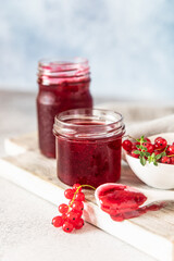 Homemade red currant jam or jelly in glass jars and red currants fresh berries on wooden cutting board.