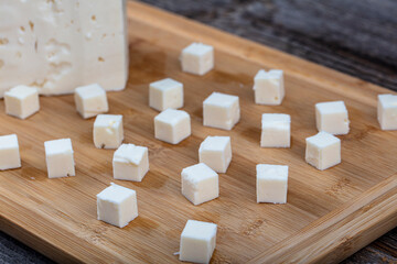 Feta Cheese Cubes on wooden cutting board. Square cubes of feta cheese isolated on wood board with...