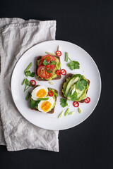 Delicious toast with guacamole, avocado, tomatoes, cucumbers and eggs on a black background