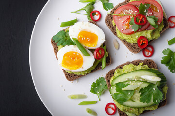Fototapeta na wymiar Delicious toast with guacamole, avocado, tomatoes, cucumbers and eggs on a black background