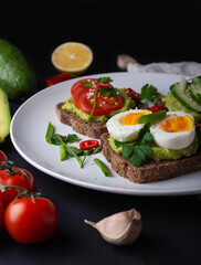 Delicious toast with guacamole, avocado, tomatoes, cucumbers and eggs on a black background