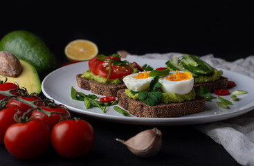Delicious toast with guacamole, avocado, tomatoes, cucumbers and eggs on a black background