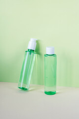 Green cosmetic bottles with face washing gel and tonic on green background. Natural organic cosmetics concept. Front view, mock up