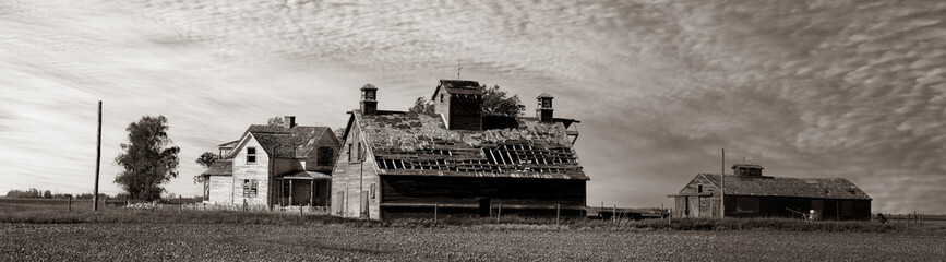 Grayscale shot of old farmhouses under the cloudy sky