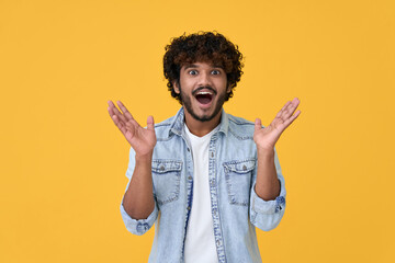 Amazed excited young indian man looking at camera with wow face expression feeling surprised advertising shopping promotion, unbelievable betting win standing isolated on yellow background. - obrazy, fototapety, plakaty