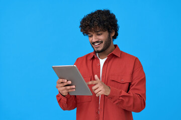 Happy indian young man using digital tablet isolated on blue background. Smiling ethnic student guy...