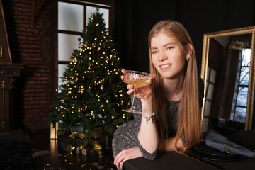 Happy blonde woman with vintage glass of champagne on dark background with christmas tree lights