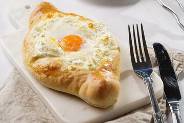 Traditional georgian dish of cheese-filled bread adjarian khachapuri with fried egg on a marble board