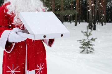 White pizza box in the hands of Santa Claus in white mittens, with a beard, in a red coat. Christmas fast food delivery. New year's eve promotion. Work on public holidays catering. Copy space, mock up