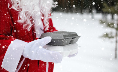 Food delivery service containers in hands of Santa Claus outdoor in snow. Christmas eve promotion. Ready-made hot order, disposable plastic box. New year holidays catering. Copy space, mock up