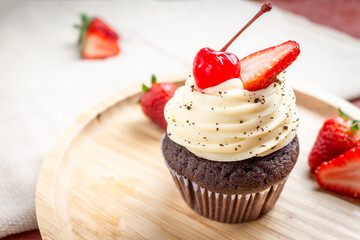 Muffin with strawberries and cherry on a bamboo plate.