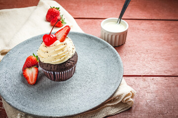 Muffin with strawberries and cherry on a gray stone plate.