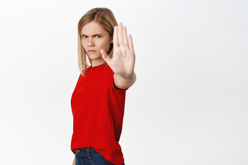 Serious little kid, girl extends one hand, shows stop, taboo or block gesture, prohibit and say no,...