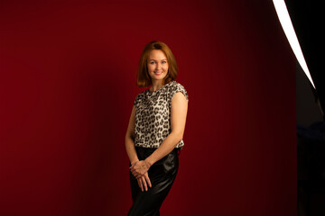 a modern stylish girl with golden hair in leather trousers and a spotted blouse on a red background