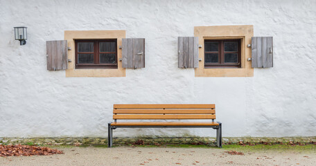 One wood bench under two windows of an old house