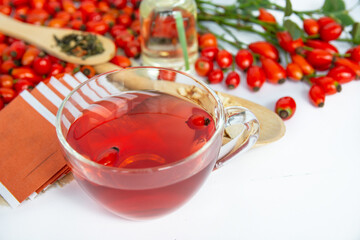 Dog rose, bunch branch Rosehips, types Rosa canina hips, essential oil and hot herbal tea cup on white background. Medicinal plants and herbs composition