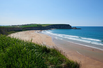 Fototapeta na wymiar A beach surrounded by cliffs and vegetation under a clear sky.