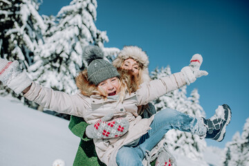 mother and daughter play in beautiful winter landscape and the mother carries the child through the air.