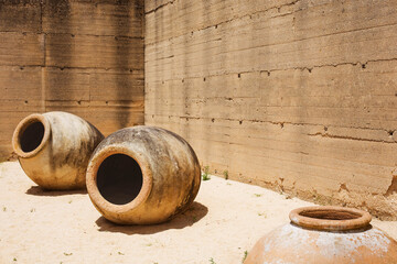Three huge antique clay jugs are on the sand against the background of an old wall. Copy space.