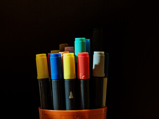 Fototapeta premium Colored felt-tip pens with caps in an orange bucket on a dark background