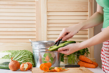 Woman peels cucumber and throws vegetable peeling, scraps in compost bucket. Food garbage reduce....