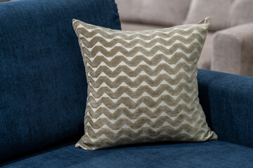 beige pillow with a zigzag pattern lies in the corner on a blue comfortable sofa in the living room