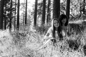Two teengirl sisters sitting on the grass in the park at summer. Black and white photo.