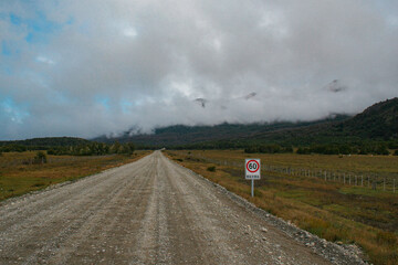 Camino desolado de ripio. Ruta de cordillera. Cielo celeste con nubes tupidas y bajas entre...
