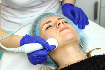 Obraz na płótnie Canvas Beauty salon. A cosmetologist in medical gloves and protective mask doing a hydra peeling procedure on the client's cheeks. Side view. Close up. Professional skin care during coronavirus pandemic.