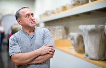 Positive smiling elderly man looking with interest at ancient sculptures in museum