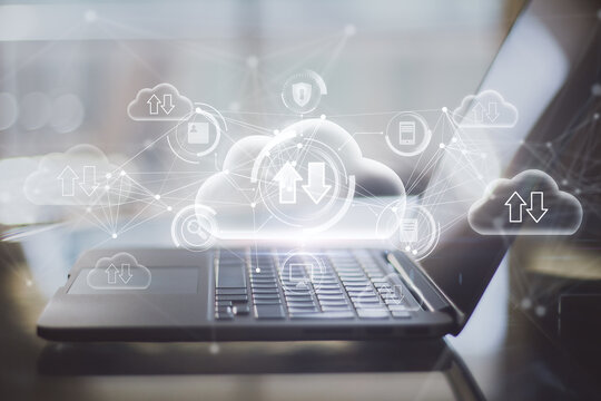 Close up of laptop on desktop with abstract glowing cloud computing hologram with download/upload arrows on blurry background. Database, technology and future concept. Double exposure.