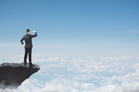 Abstract image of businessman looking into the distance while standing on edge of cliff, mock up place on sky with clouds background. Success, challenge, future and growth concept.