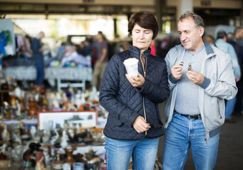 Cheerful man and woman choosing interesting souvenirs at traditional flea market
