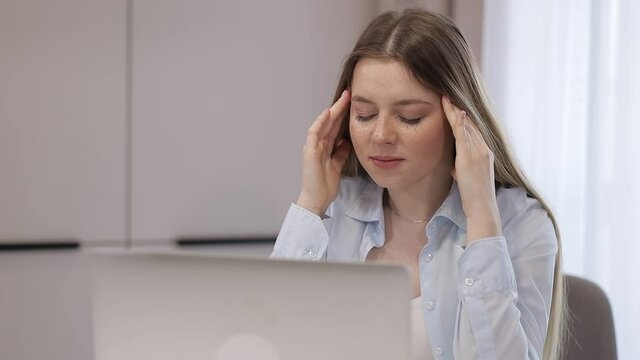 Tired overworked woman workaholics sit at work desk in modern office using laptop, working on deadline assignment, urgent project feeling tired, headache, migraine