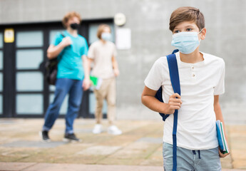 Teen boy in face mask with backpack going to home after finishing lessons at school on sunny day