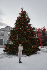 The girl looks at the decorated Christmas tree in the city square. Festive new year lights and...