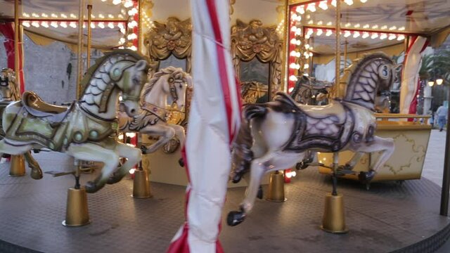 Carousel with galloping horses at amusement park or fairground, designed for kids to play and have fun. Children riding wooden animals on slowly rotating merry-go-round.