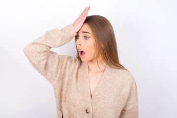 young caucasian girl wearing knitted sweater over white background surprised with hand on head for...