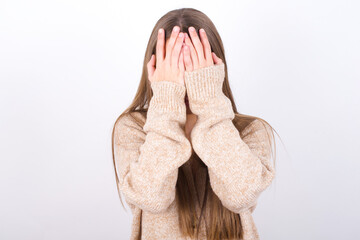young caucasian girl wearing knitted sweater over white background covering her face with her hands, being devastated and crying. Sad concept