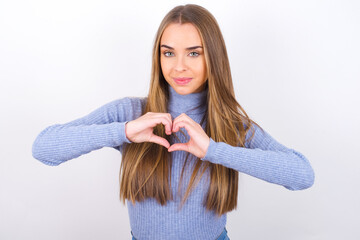 Serious Young caucasian girl wearing blue turtleneck over white background keeps hands crossed stands in thoughtful pose concentrated somewhere