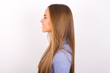 Profile portrait of nice Young caucasian girl wearing blue turtleneck over white background look empty space toothy smile