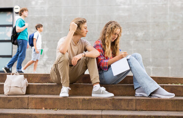 Fototapeta premium Boy and girl teens preparing for exams while sitting on stairs outdoors near school building.