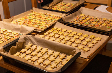 christmas cookie baking session - view over the kitchen table with several pans of christmas cookies, partly already decorated with sugar coating 
